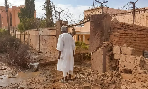 A man walks through rubble by a bullet-riddled wall