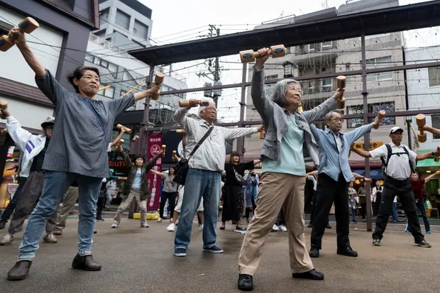 People exercise with wooden dumbbells during an event marking